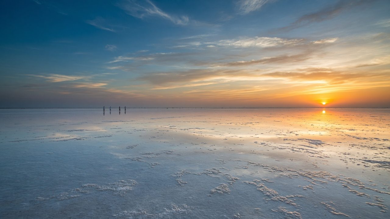 The white salt flats of the Rann of Kutch at sunset, sky and shallow water glowing orange and teal
